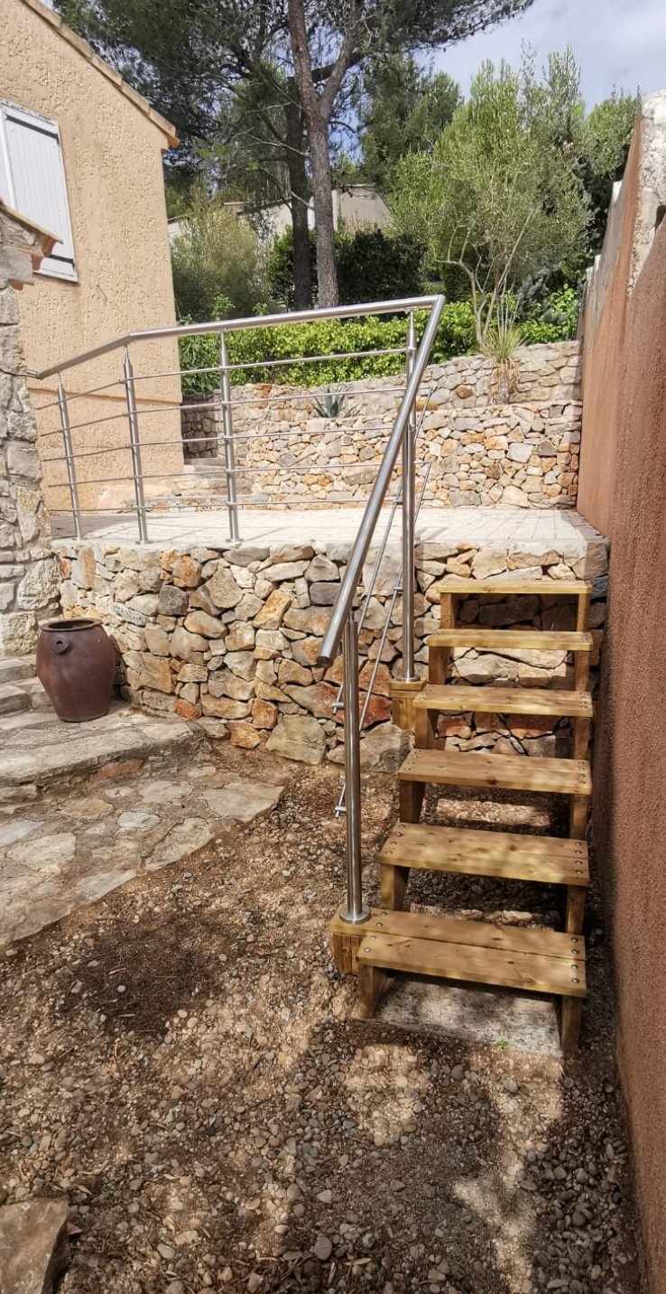 Mur en pierre avec terrasse surélevée, escalier en bois et garde-corps en inox, aménagé sur un terrain en dénivelé proche d’Aubagne.